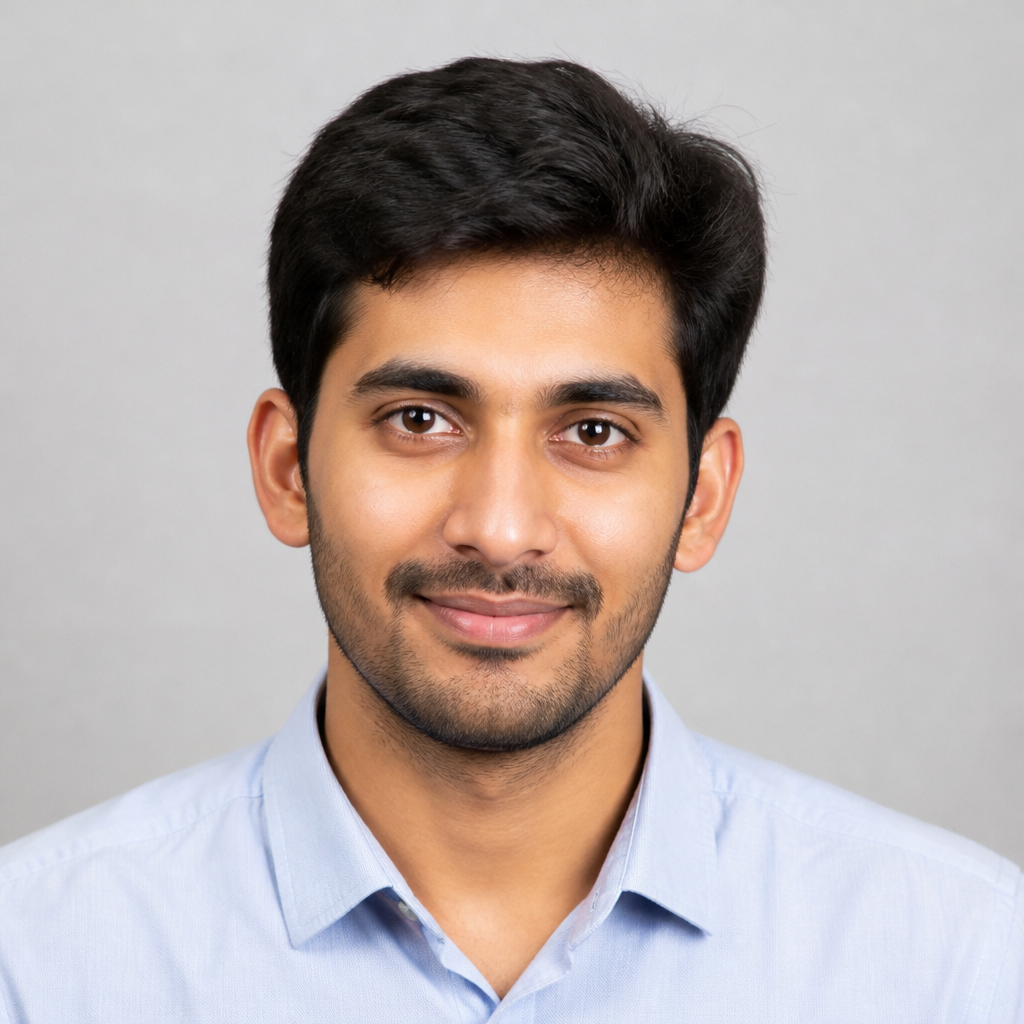 Smiling Indian man with warm brown complexion, short dark hair, soft natural window light, relaxed friendly portrait against a blurred muted backdrop