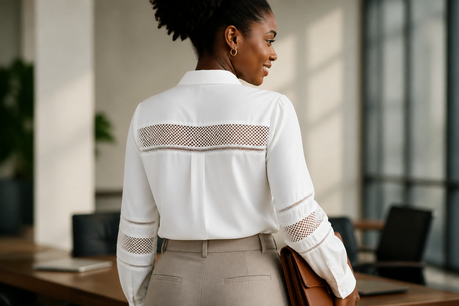 African businesswoman wearing a crisp white Ladies T-Shirt tucked into high-waisted tailored trousers in a modern bright office, holding a leather portfolio with confident smile