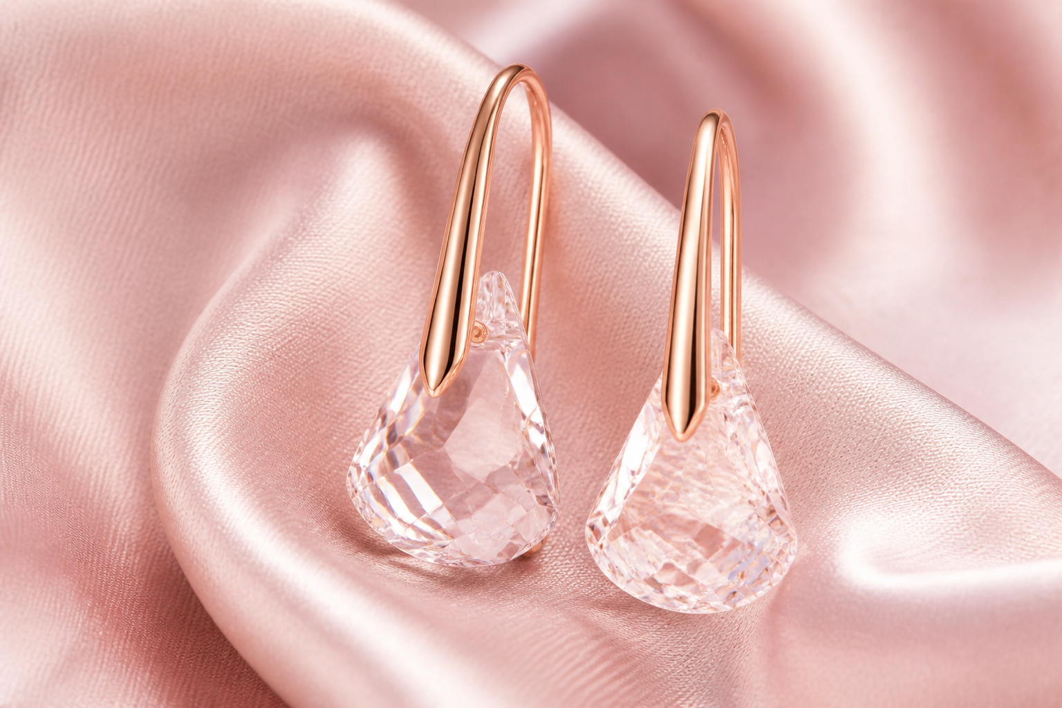 Macro product shot of the pink Lunar drop earrings with Toupie cut crystals suspended on a soft pink satin fabric backdrop, soft natural studio lighting highlighting the rose gold finish and crystal facets