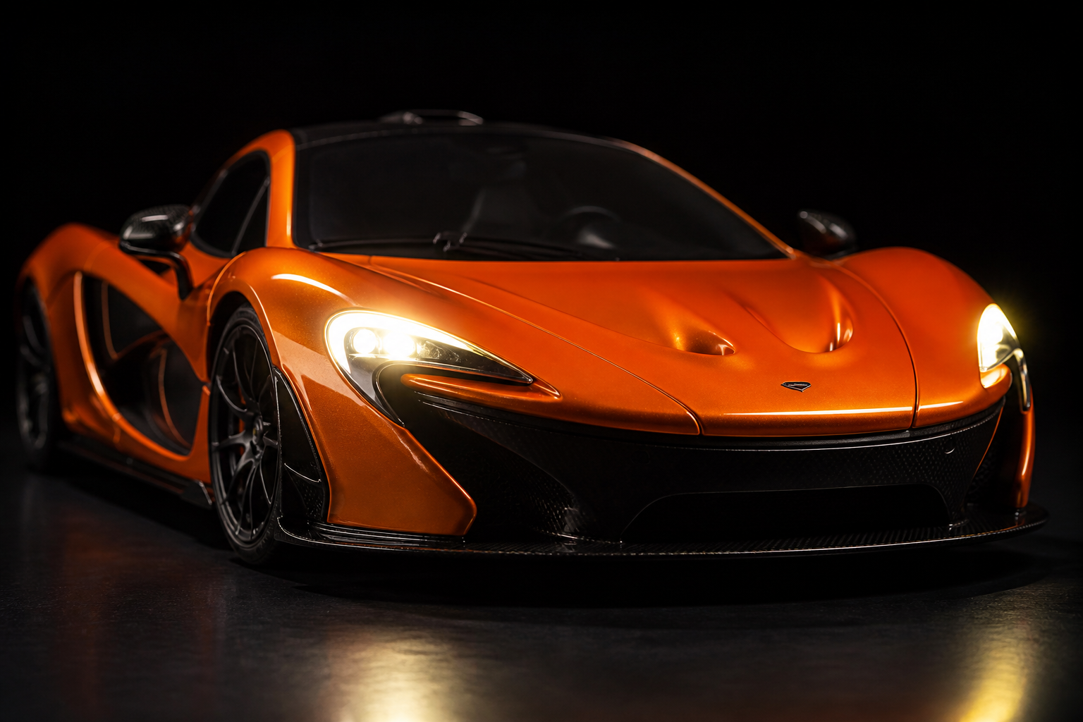 Close-up product shot of a 1:14 scale McLaren P1 RC car with bright LED headlights glowing warmly on a sleek black surface, dramatic low-key lighting highlighting every body line