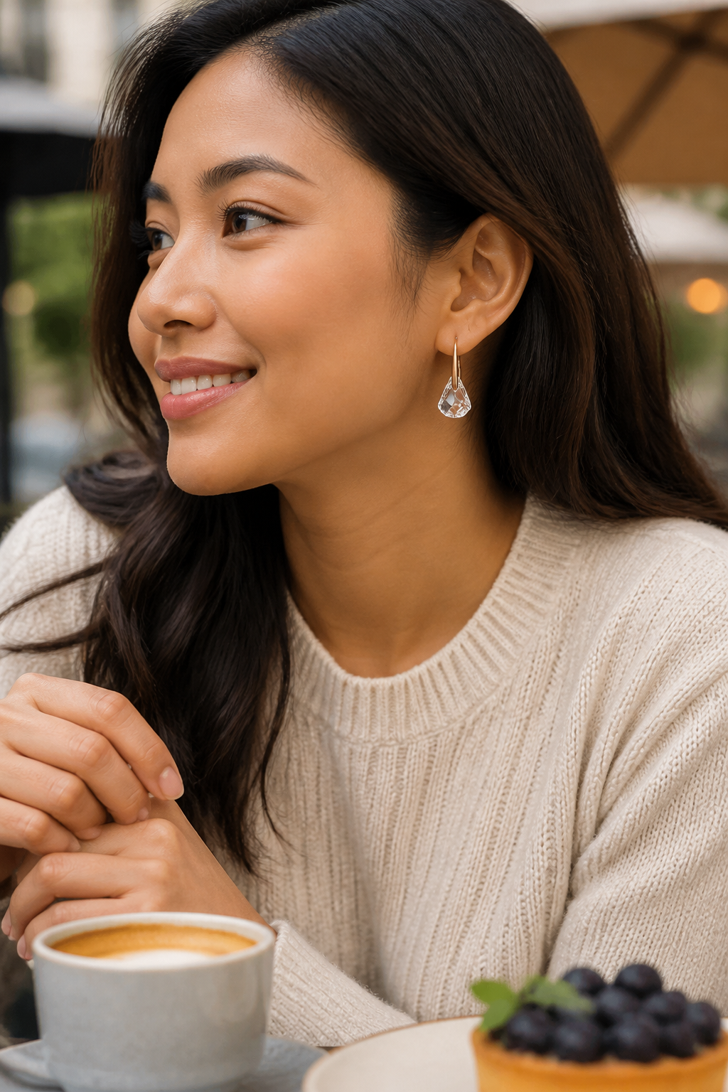 Casual weekend brunch lifestyle photo of a Southeast Asian woman in a soft sweater wearing Lunar Drop earrings at an outdoor cafe