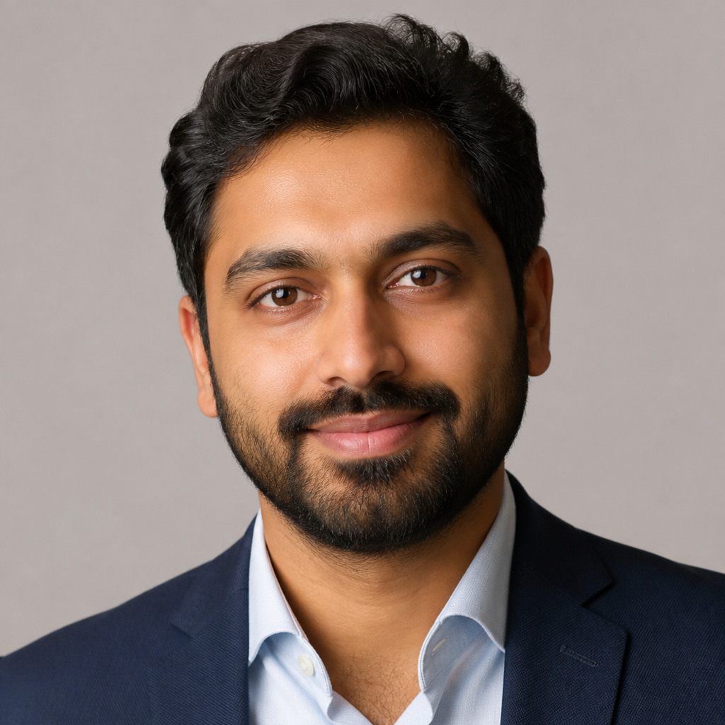 Close-up portrait of a young Indian man with short dark hair, light stubble, friendly relaxed smile, soft natural window light, neutral background