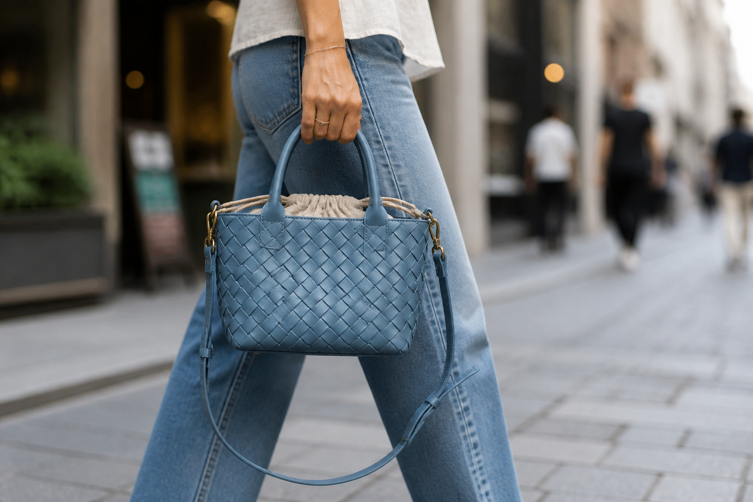 Model holding the Mini Azure woven tote by its top double handles on a city street, looking polished and ready for a daytime outing in soft natural light