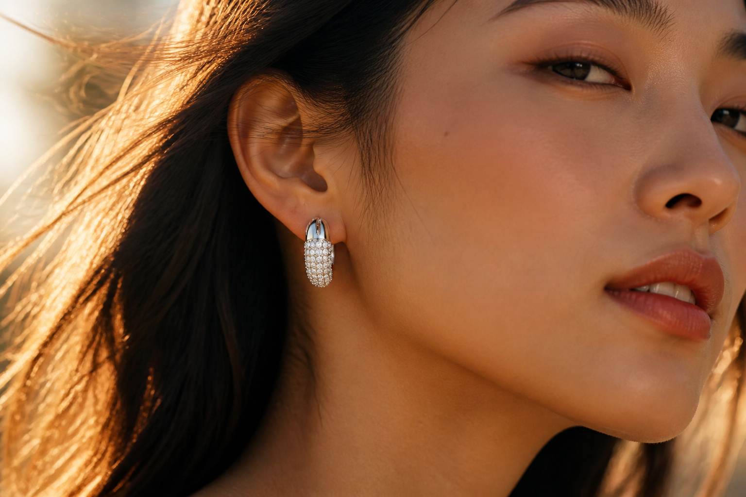 Cinematic close-up of a young Asian woman wearing the Dextera hoop earrings in white 18K gold finish, soft golden hour lighting, glistening pav&eacute; crystals catching the light
