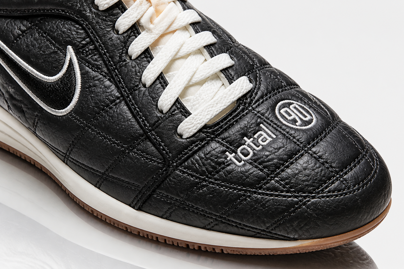 Extreme close-up macro shot of the Nike Total 90 Premium quilted leather upper showing the signature stitching pattern and asymmetrical lacing system in sharp studio lighting