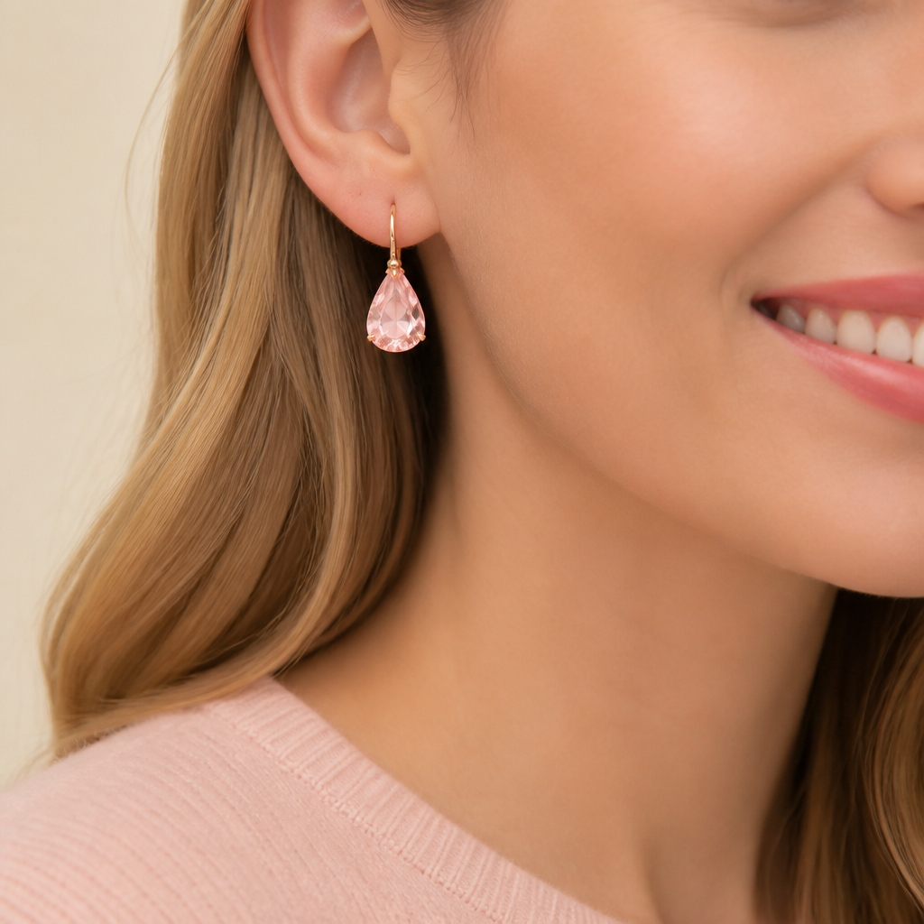 Close-up of the pink Lunar drop earrings hanging, catching soft pink light on a clean cream background