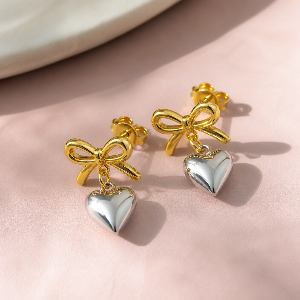A pair of Love Heart Earrings in rose gold and silver finish on a clean light pink surface, soft daylight, product photography style=