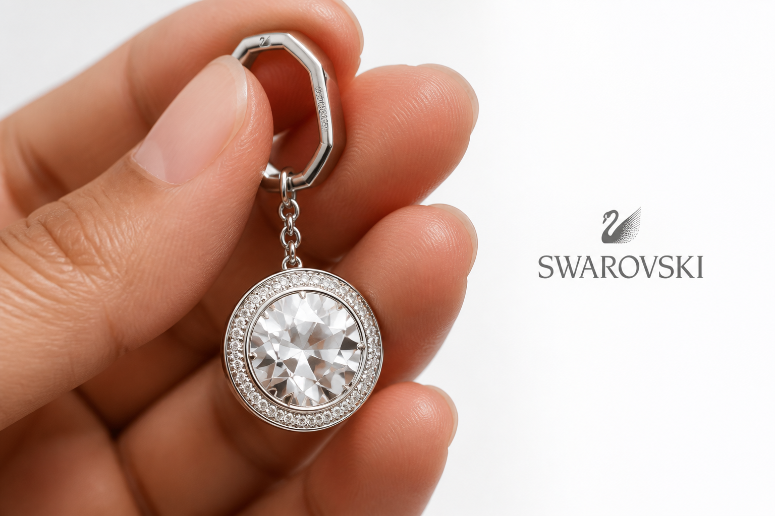 Close-up macro shot of the official Swarovski swan logo engraved on rhodium plated metal, displayed alongside the brand's signature blue packaging box with crystal paper