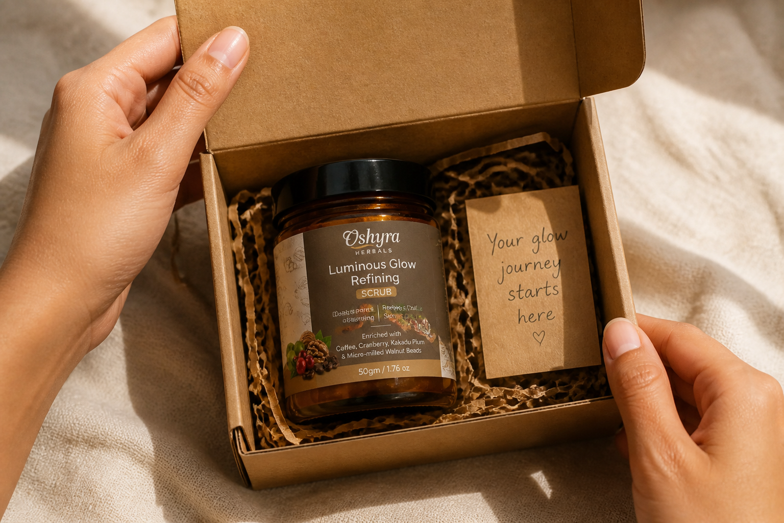 Hands opening a kraft paper delivery box revealing the Oshyra Herbals 50g amber glass jar with a small handwritten note tucked beside it, soft natural daylight, linen tablecloth background, intimate unboxing moment
