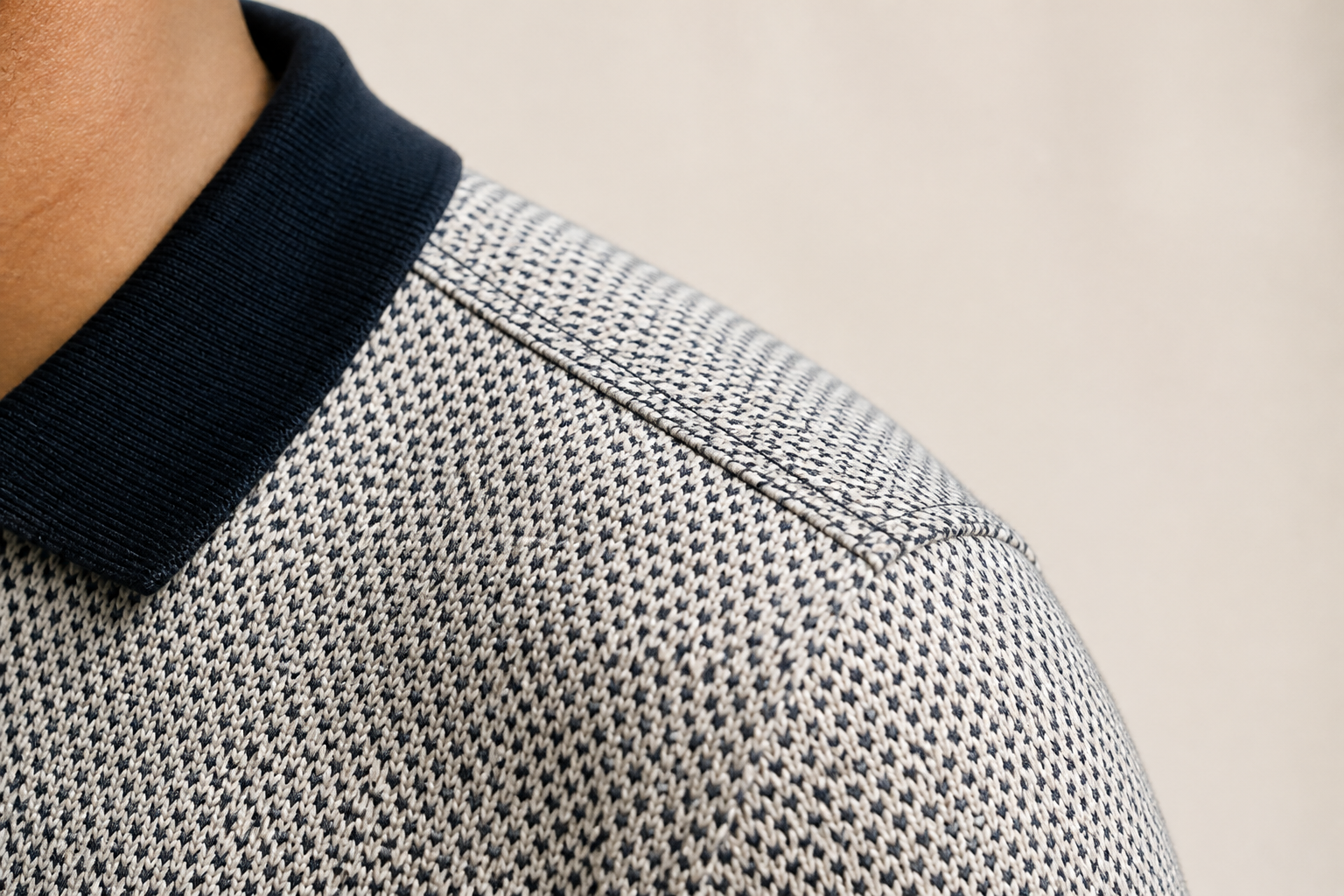 Macro shot of fine double-stitching detail on the shoulder seam of the Posh Monk polo on cream background