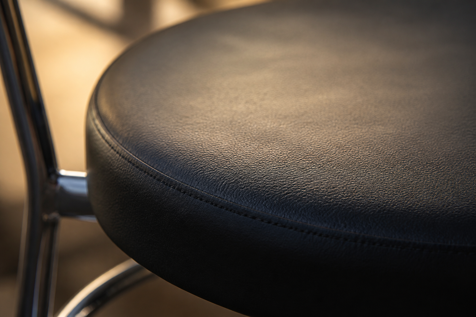 Macro close-up photograph of the soft black cushion on the steel chair showing texture, fabric weave and quilting detail under warm natural light.
