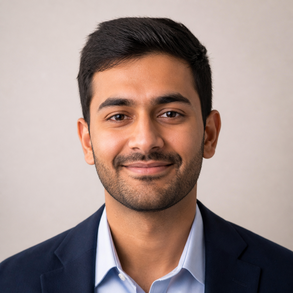 Close-up portrait of a confident Indian man in his late thirties, short beard, warm smile, wearing a smart casual shirt in a softly lit modern office