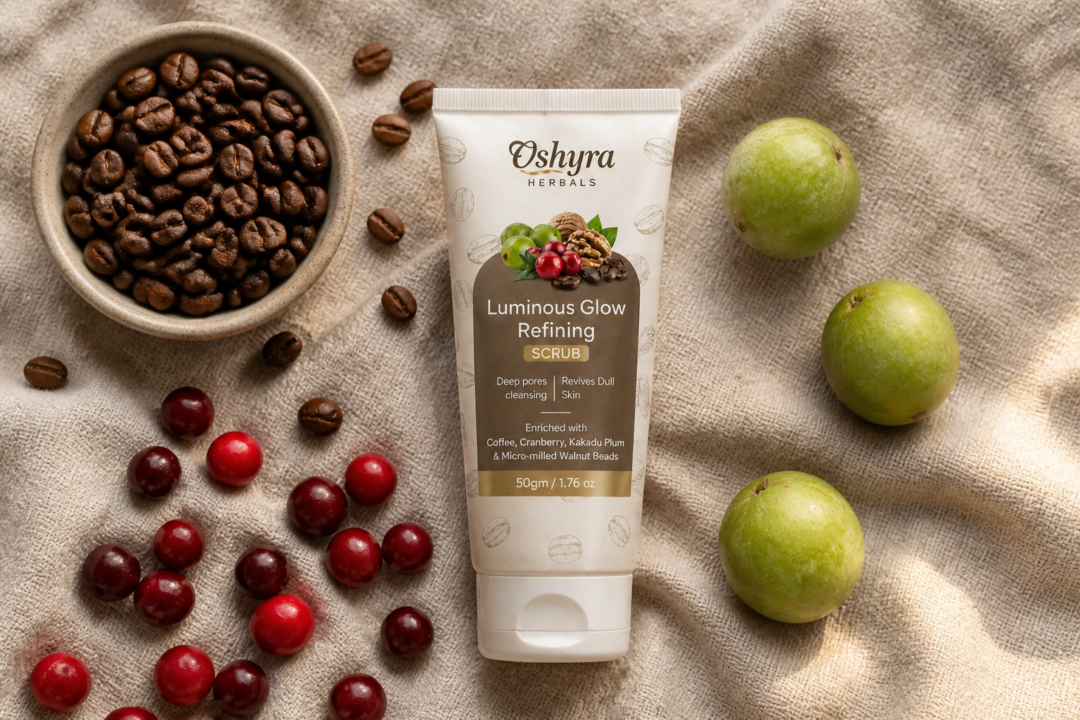 Flat-lay storytelling shot of three raw natural ingredients arranged on linen fabric: roasted coffee beans in a small ceramic bowl, fresh red cranberries scattered, and three small Kakadu Plum fruits, with the amber glass scrub jar open in the center showing the brown coffee scrub texture