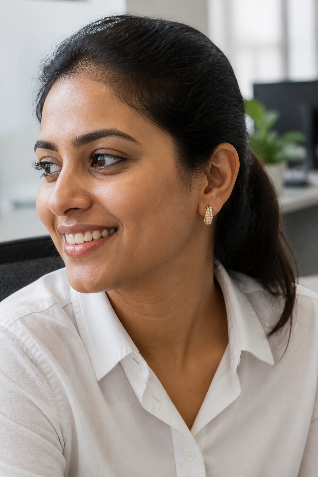 Young Indian woman in a crisp white shirt at her office desk wearing Dextera Small gold-finish hoops, soft natural window light, candid smile