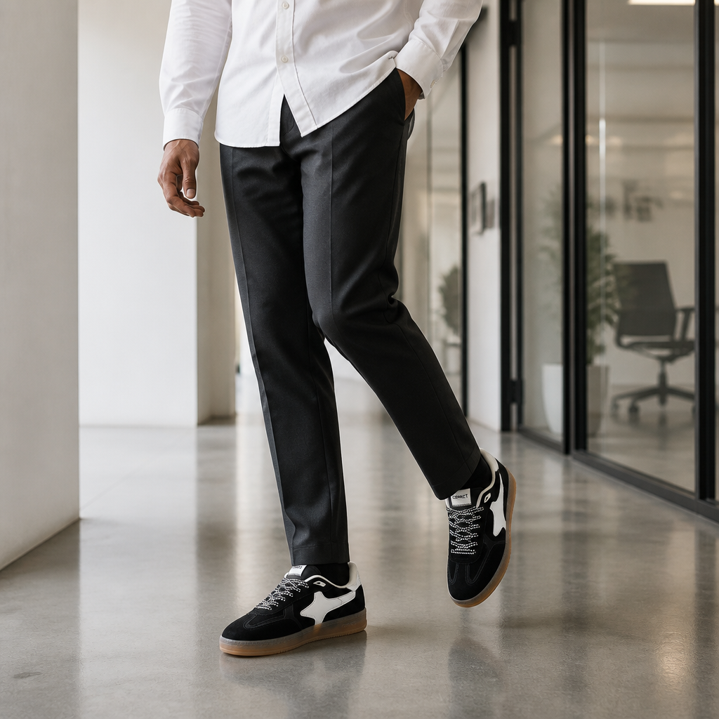 Person in tailored trousers and white shirt walking through modern minimalist office corridor wearing Aeres NOIR sneakers, professional yet relaxed