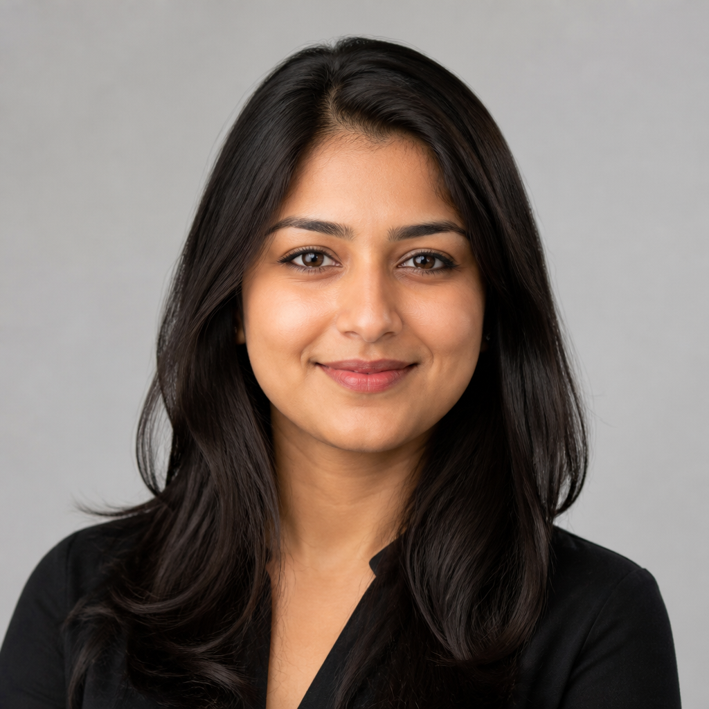 Warm friendly headshot of a smiling Indian woman in her thirties wearing a soft pink blouse with natural makeup and gentle golden light