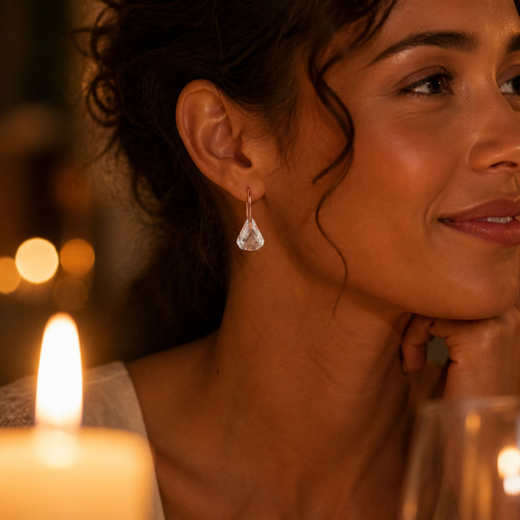 Woman wearing Lunar pink drop earrings at an intimate candlelit dinner, soft warm light reflecting off the crystals as she smiles